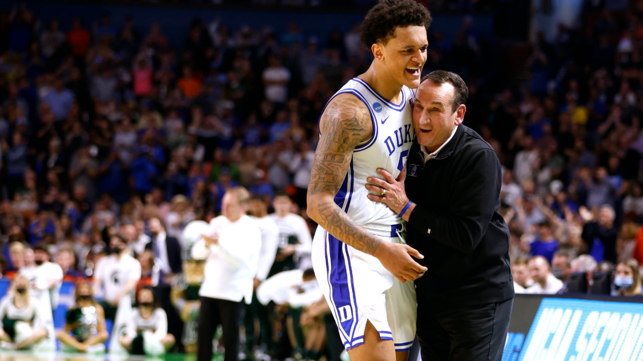 Duke University basketball coach hugging star player Paolo Banchero on the court during an NCAA Tournament game