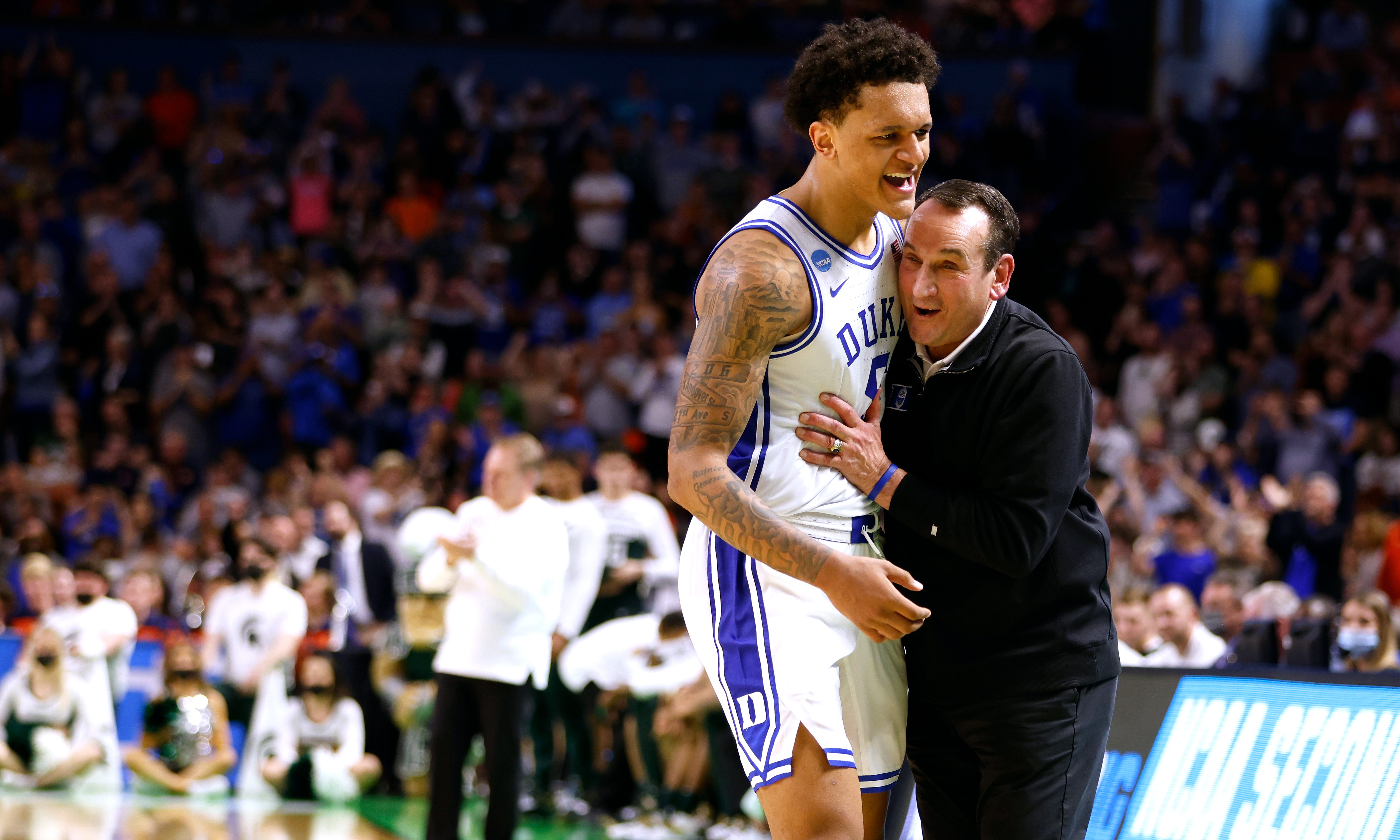 Duke University basketball coach hugging star player Paolo Banchero on the court during an NCAA Tournament game