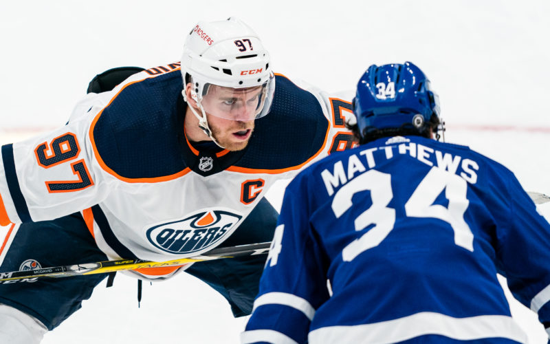 Hockey players Connor McDavid and Auston Matthews staring at each other before a face-off on the ice