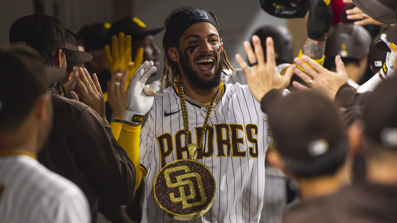 Fernando Tatis Jr. celebrating in the dugout high-fiving his teammates while wearing a Padres necklace