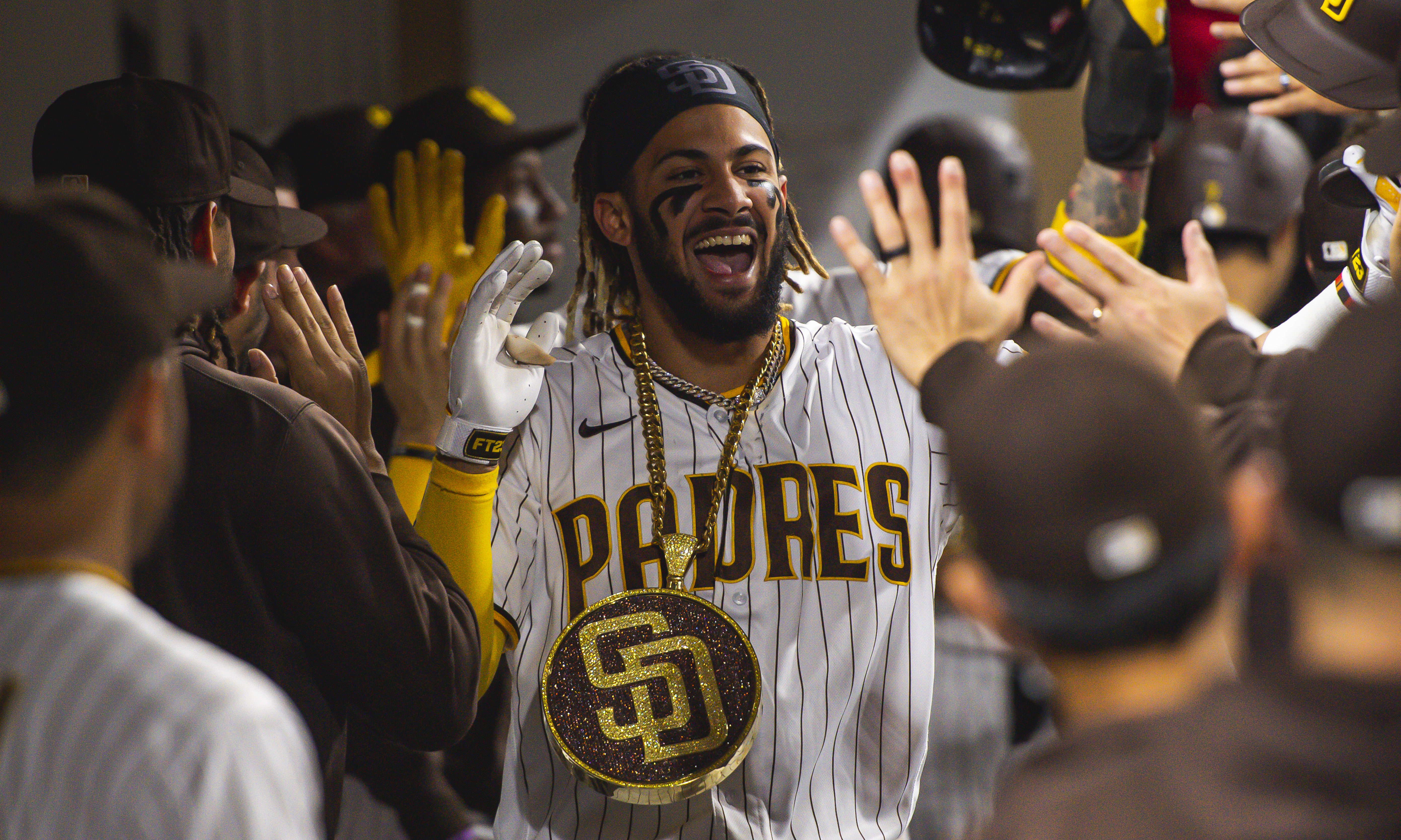 Fernando Tatis Jr. celebrating in the dugout high-fiving his teammates while wearing a Padres necklace