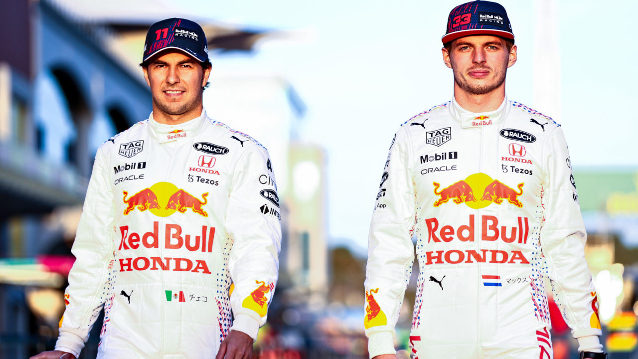 Formula 1 drivers Max Verstappen and Sergio Perez walking on a race track wearing white Red Bull jumpsuits