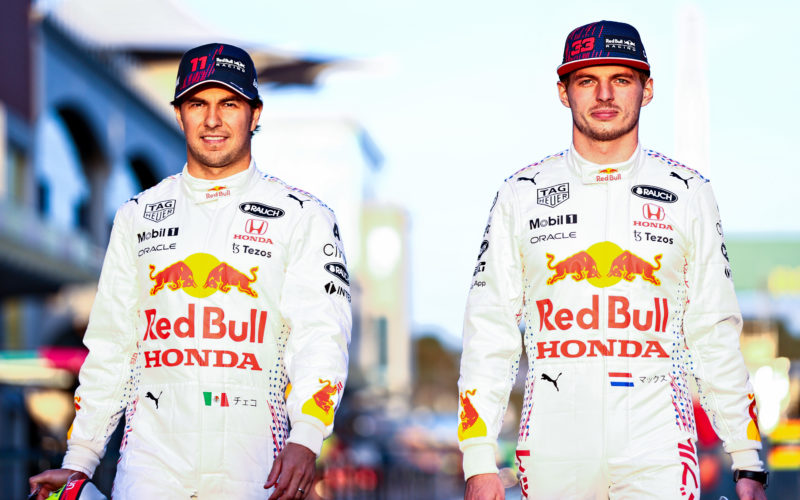 Formula 1 drivers Max Verstappen and Sergio Perez walking on a race track wearing white Red Bull jumpsuits