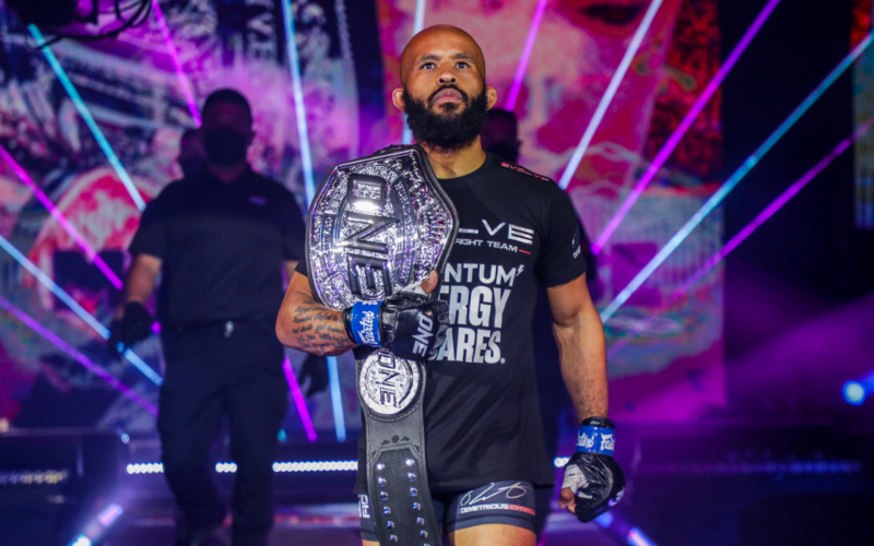 Demetrious Johnson walking down a catwalk with an MMA championship belt hanging over his right shoulder