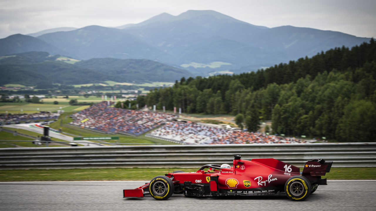 Profile view of a Ferrari Formula 1 car racing on a track with Austrian mountains in the background