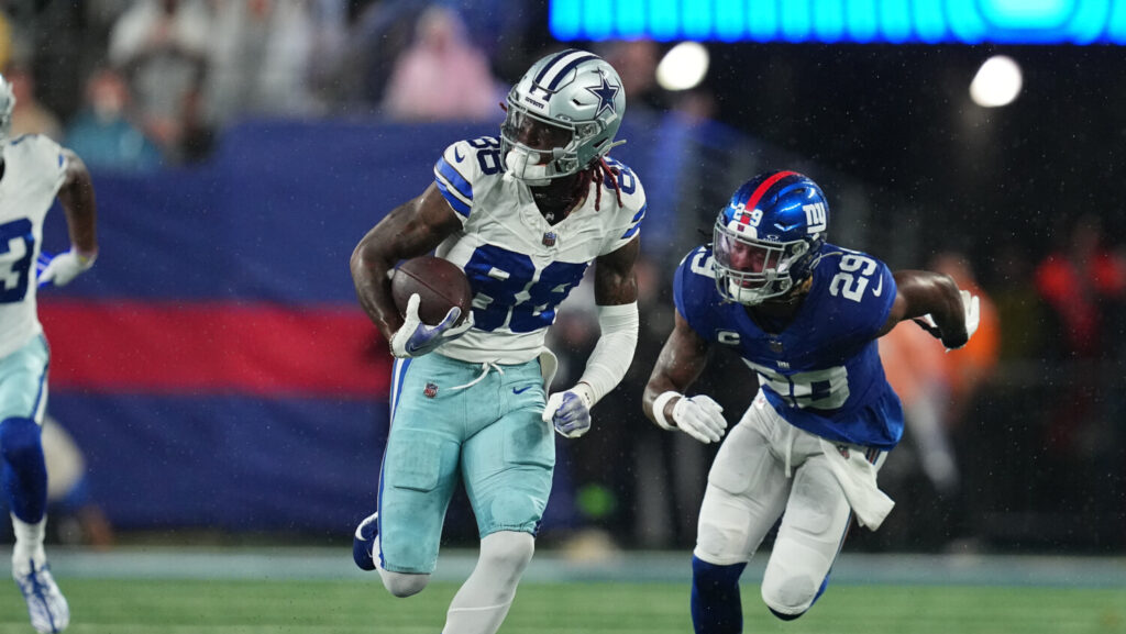 CeeDee Lamb running with a football and looking to his right while an opposing player chases him