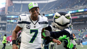 Geno Smith celebrating and smiling walking alongside the Seattle Seahawks mascot on the field after a football game